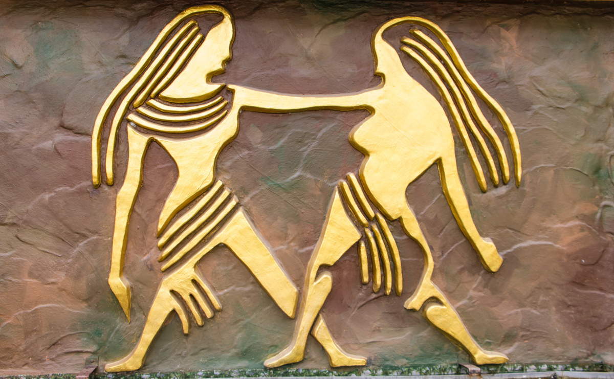 Imagem de duas silhuetas douradas e iguais, interligadas por um braço, representando o signo de Gêmeos.