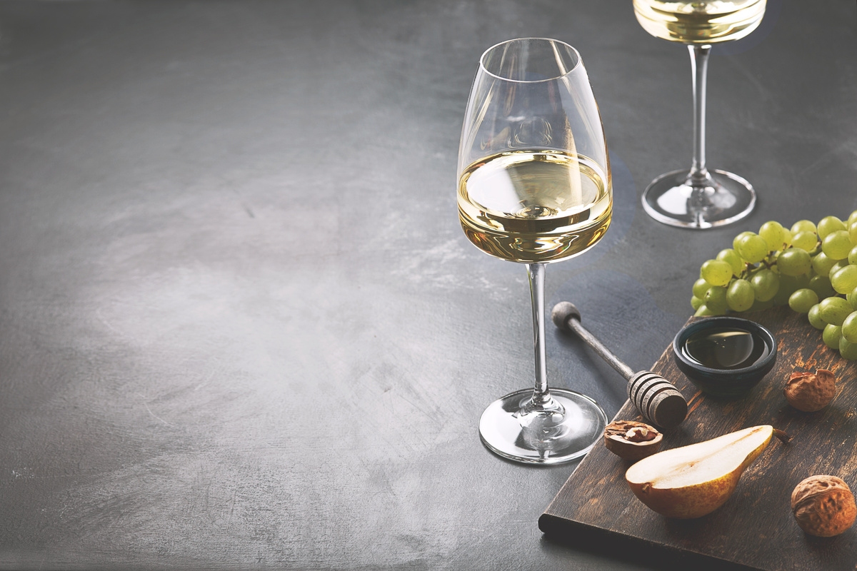 Taça com vinho branco ao lado de tábua com uvas