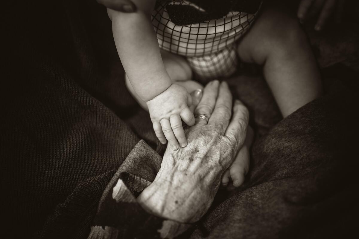 Mão de uma mulher idosa fazendo carinho nas pernas de um bebê. 