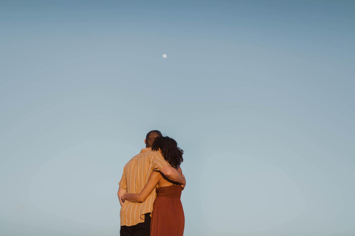 Casal abraçado de costas, olhando para a lua.