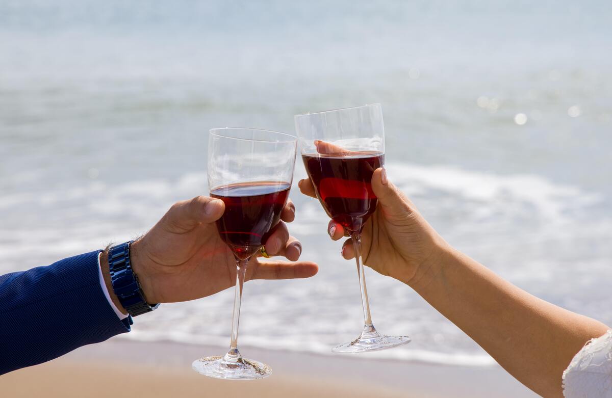 Casal brindando com taças de vinha na praia.