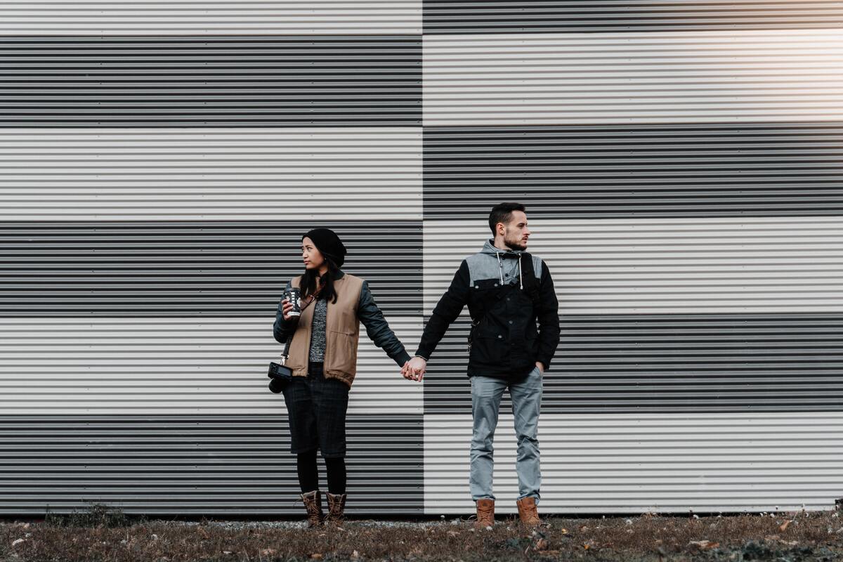 Homem e mulher em pé na frente de uma parede, de mãos dadas.