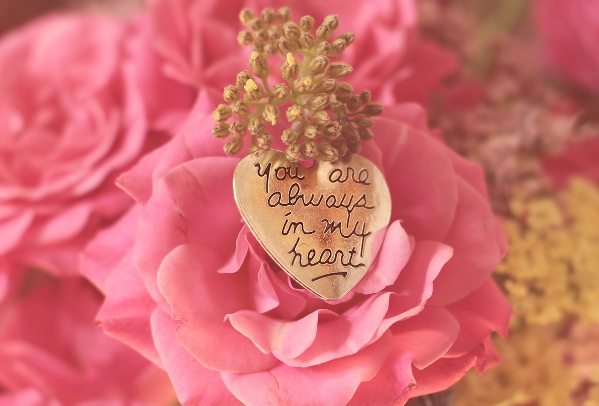 Pingente de coração feito de ouro repousado em rosa cor-de-rosa, com gravura em inglês.