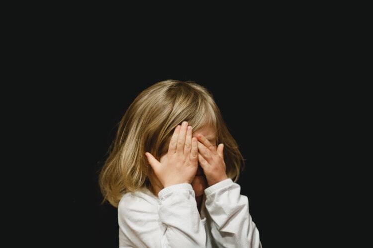 Criança escondendo o rosto com as mãos