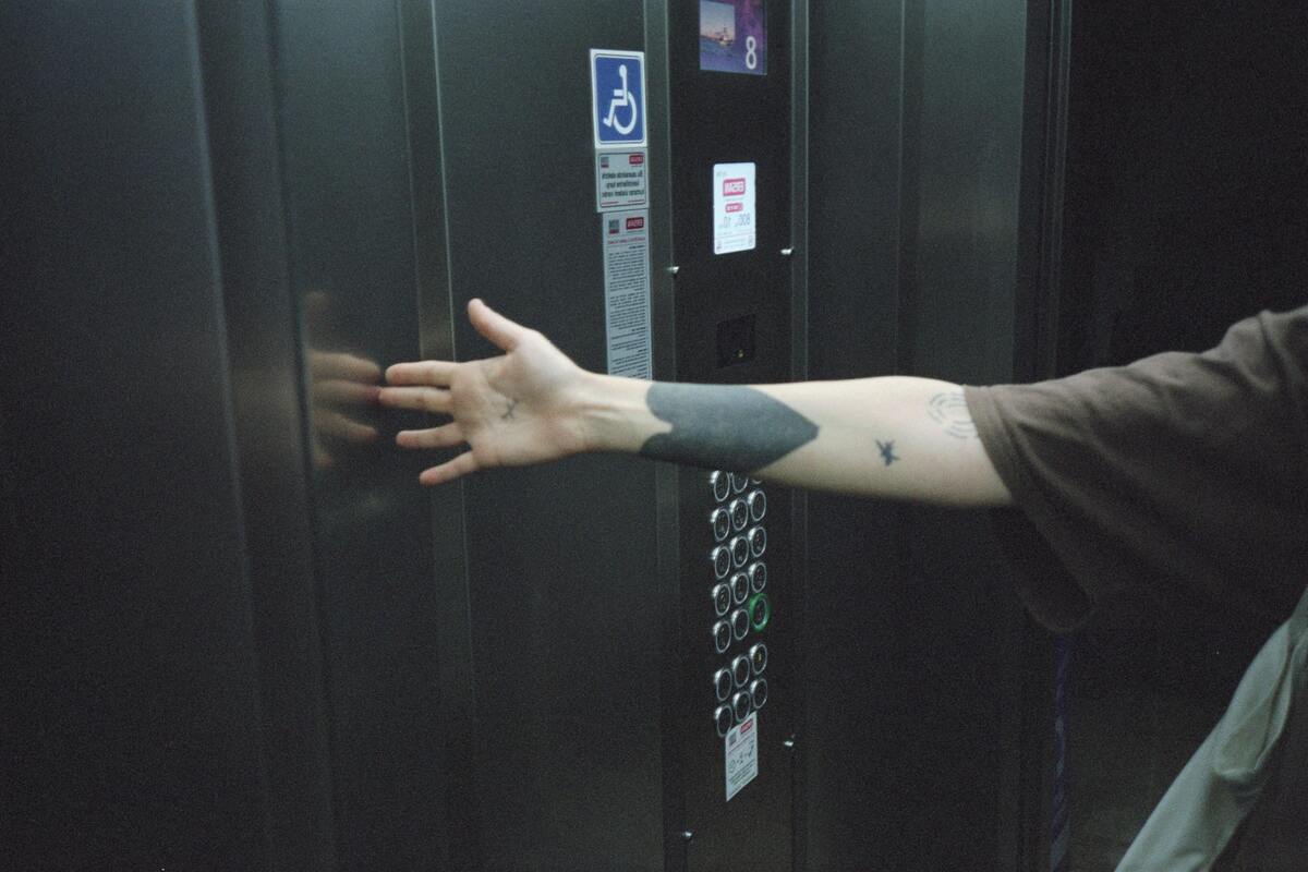 Homem dentro do elevador tocando as paredes com a mão.