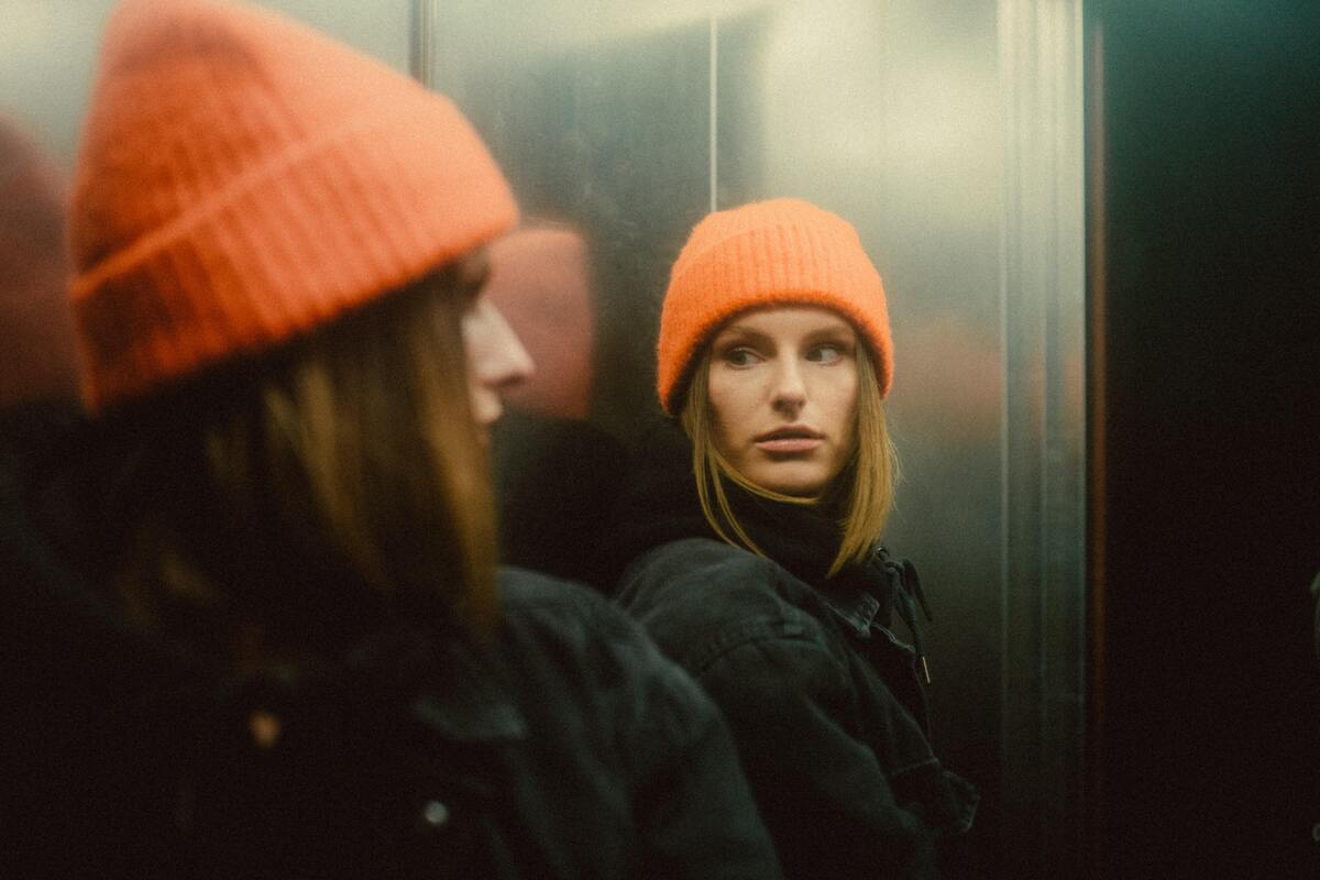 Mulher se encarando no espelho do elevador.