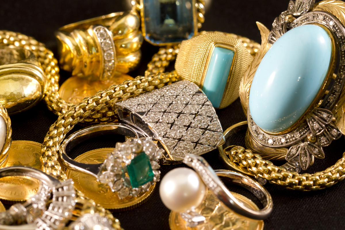 Diversas joias, como brincos, pulseiras douradas e de pedra, espalhadas por superfície preta.