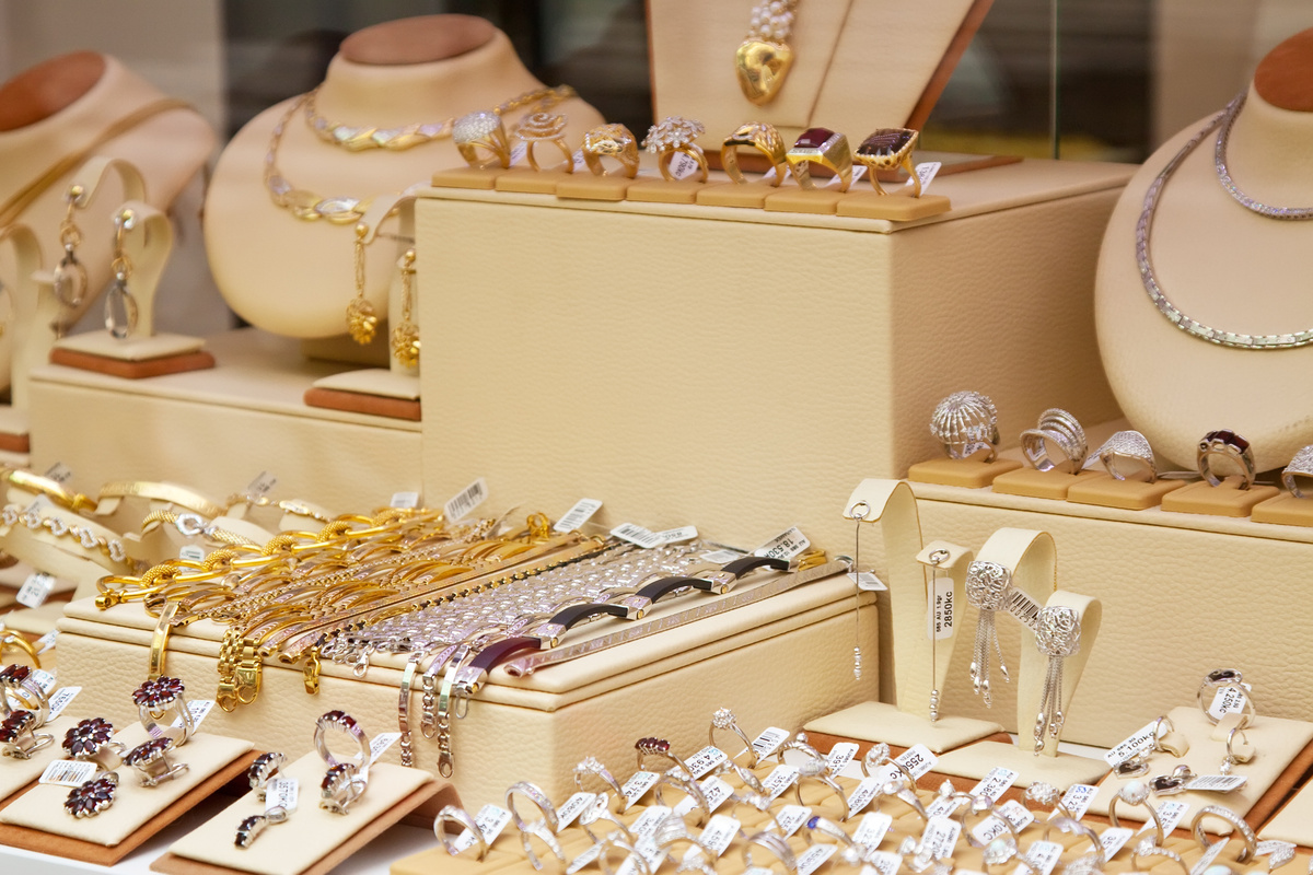 Prateleira com diversos tipos de joias em mostruário, sendo elas douradas ou pratas, colares, pulseiras ou anéis.