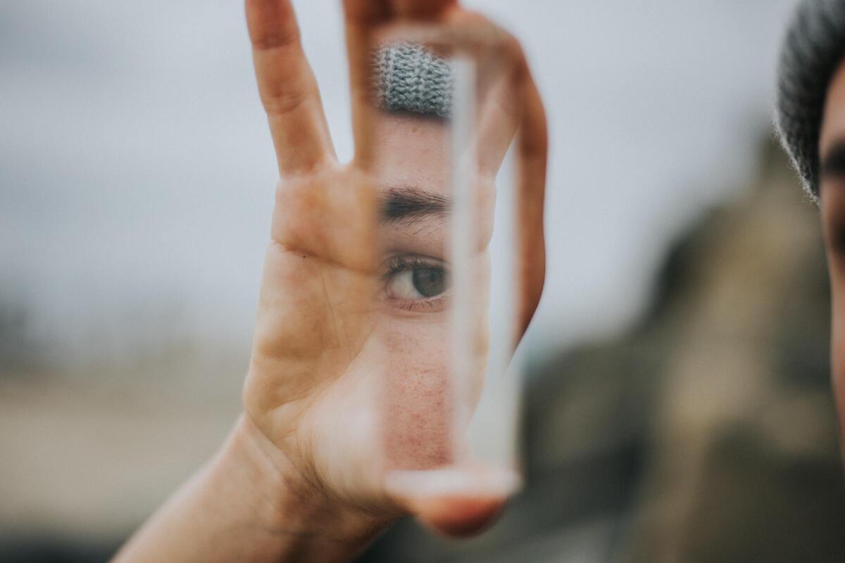 Mulher segurando um pedaço de vidro que reflete o olho de uma mulher.