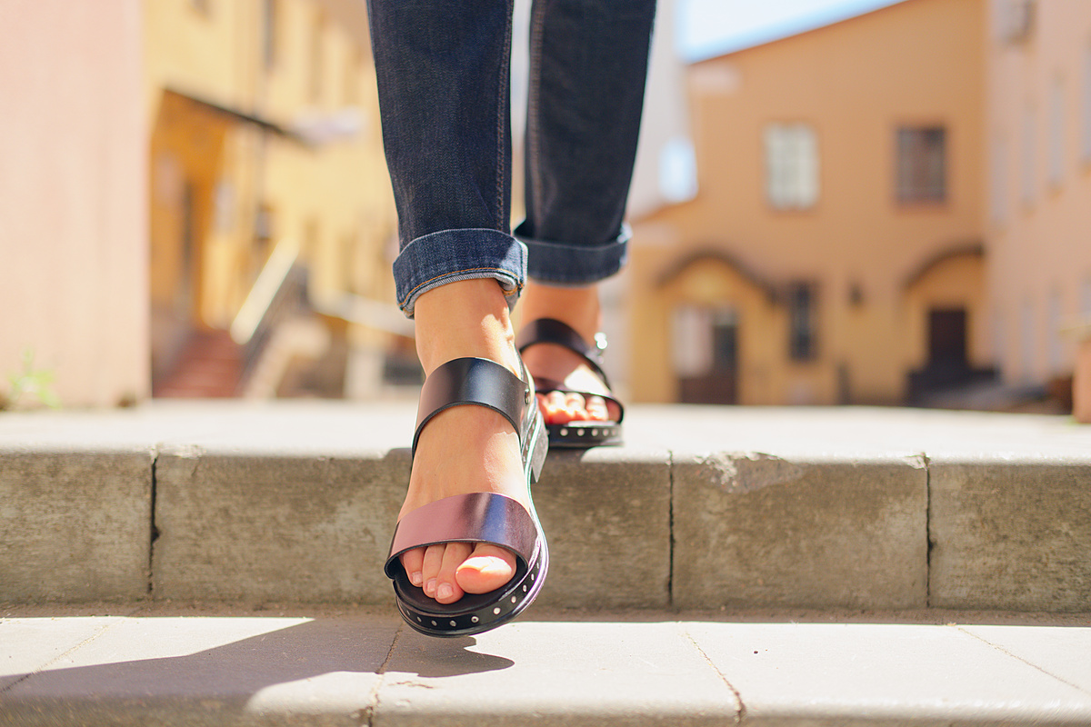 Mulher andando com sandálias pretas de couro sintético.