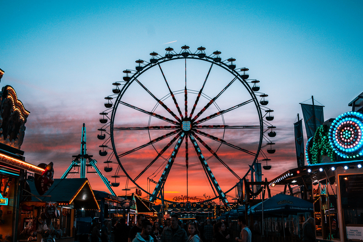 Roda gigante vista de longe, em cenário de por do sol avermelhado, dentro de parque de diversões.