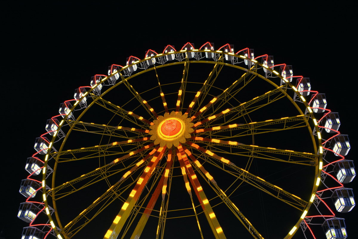 Roda gigante vista de baixo, em cenário noturno enquanto iluminada com luzes amarelas e vermelhas.