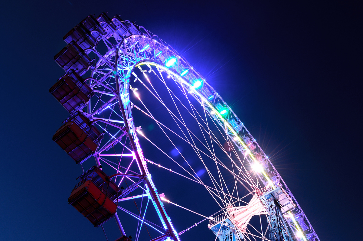 Roda gigante vista de baixo e à noite, enquanto iluminada com luzes roxas e azuis.