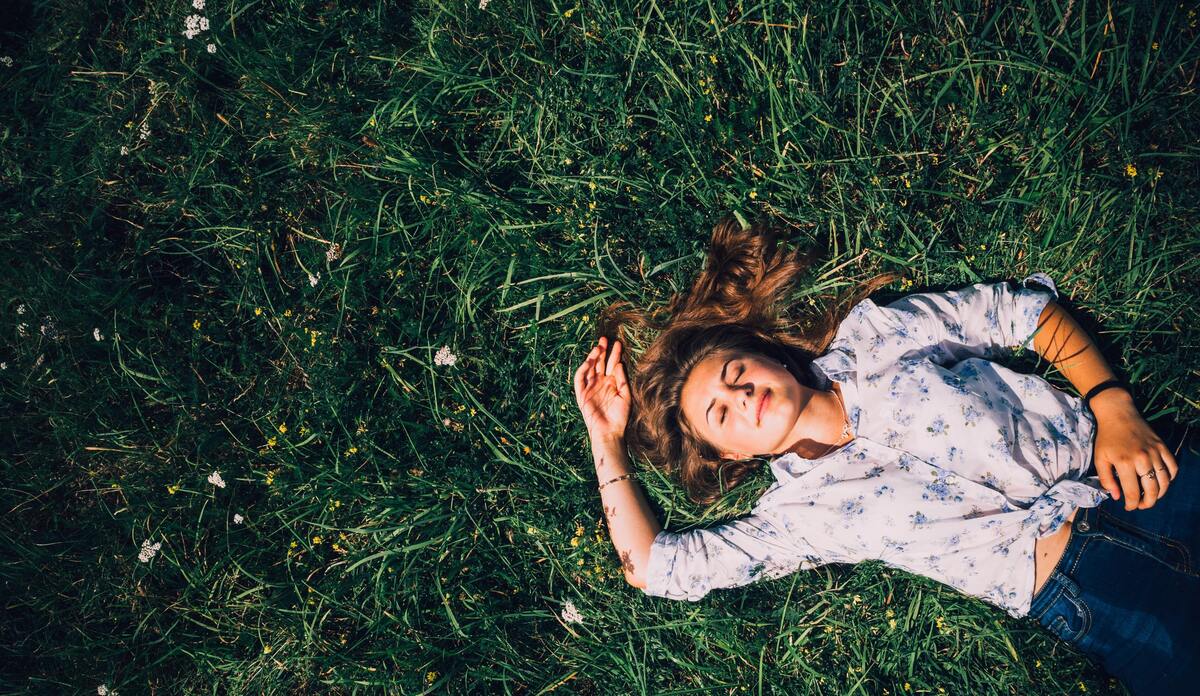 Mulher deitada em um campo gramado de olhos fechados.