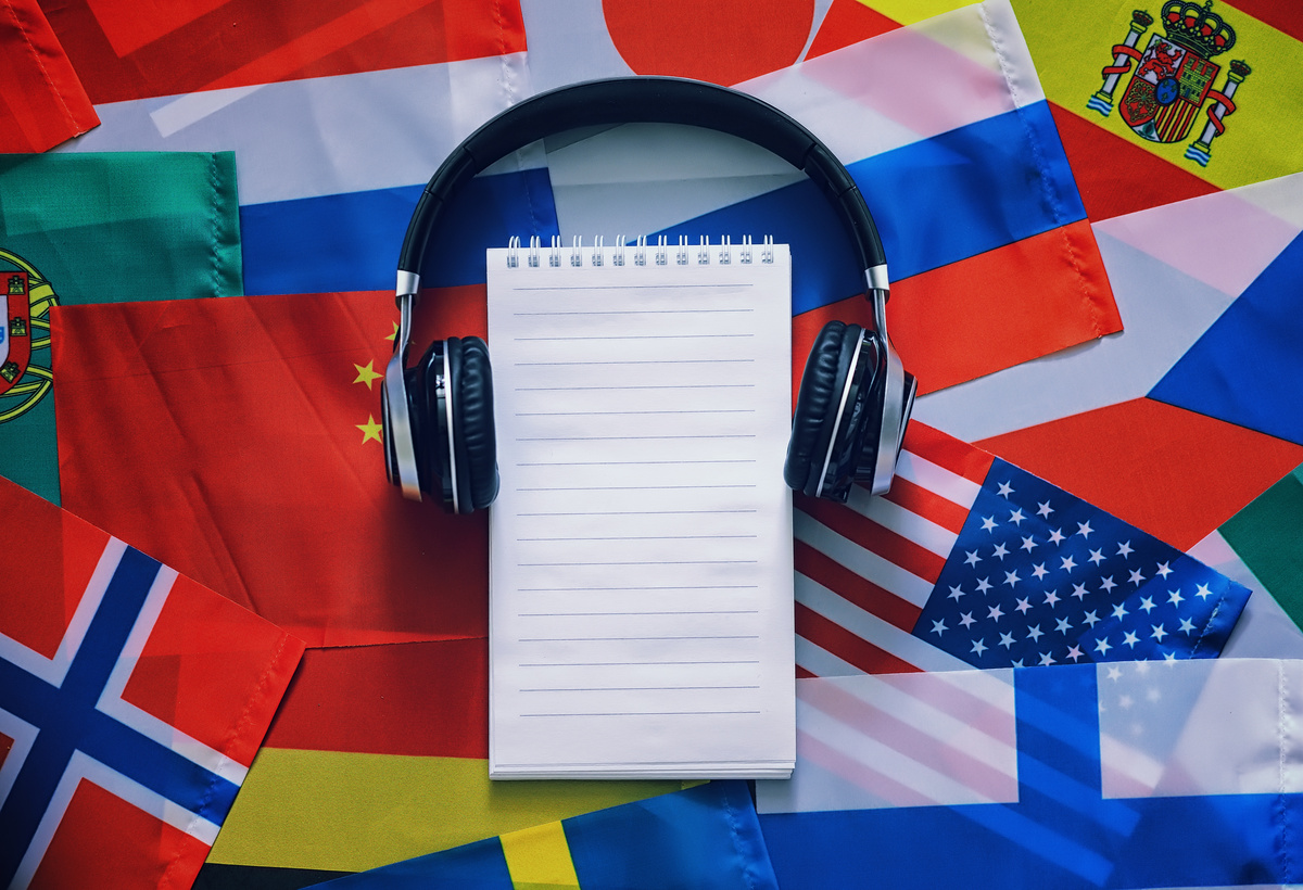 Caderno com fone de ouvido e bandeiras ao fundo; aula de idioma estrangeiro
