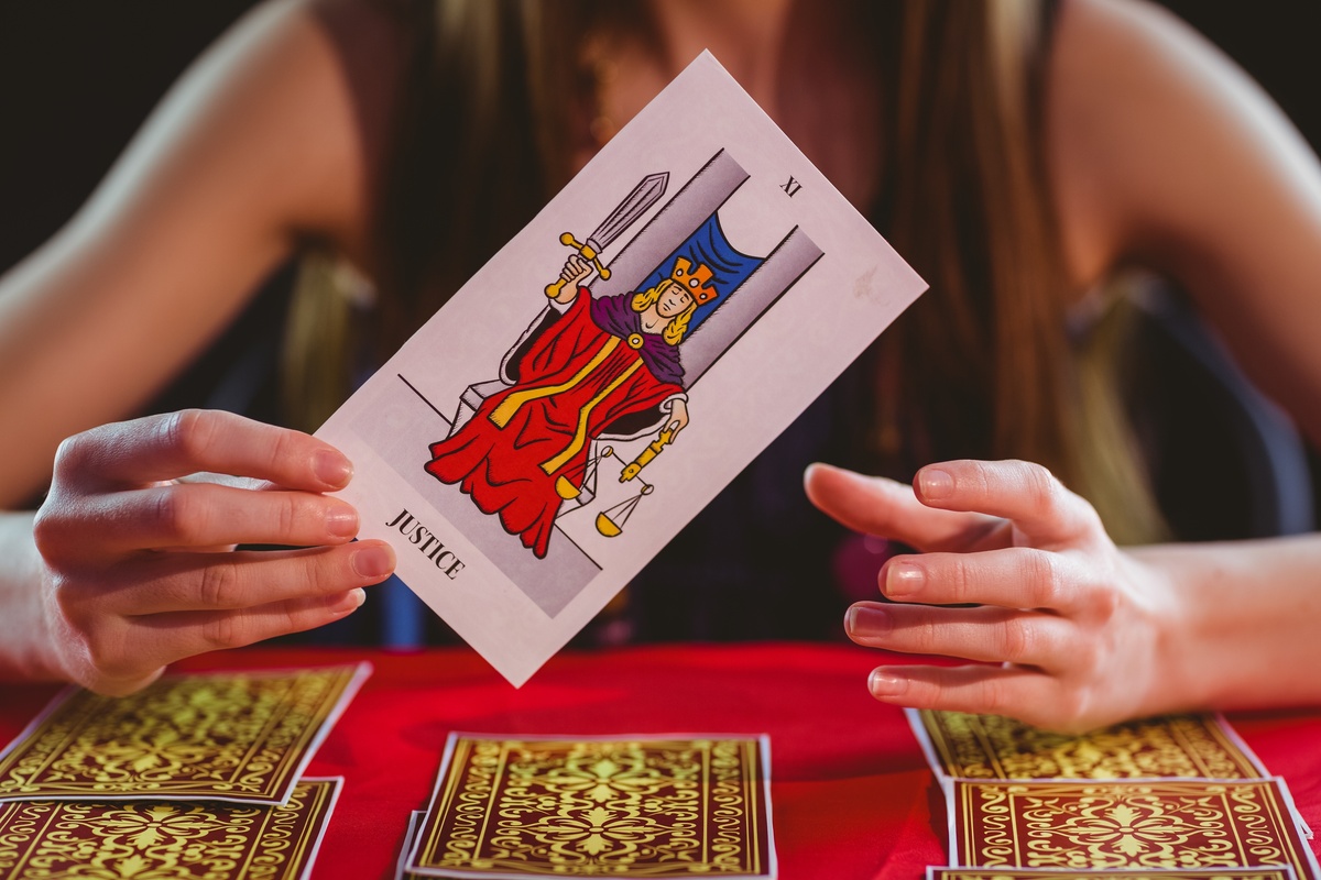 Mulher sentada de frente para mesa, mostrando carta A Justiça após tirá-la em seu baralho de Tarot.