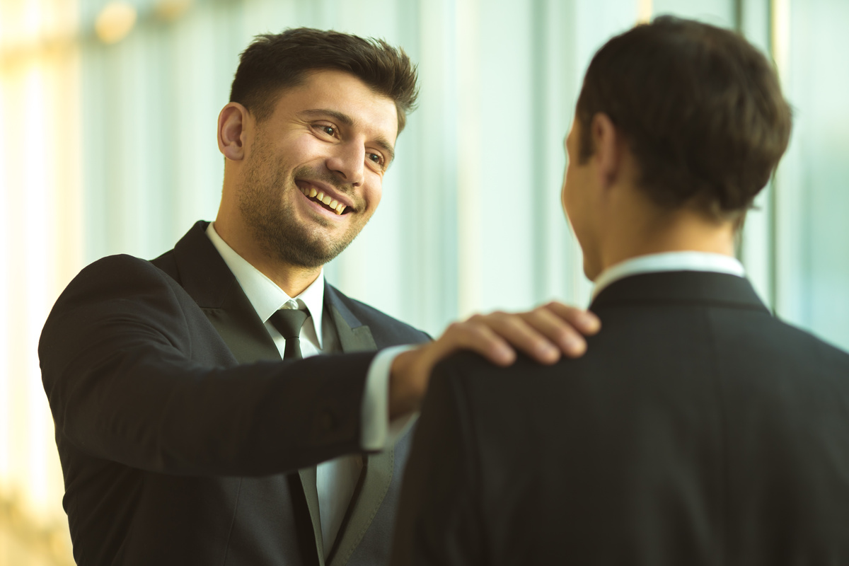 Homem sorridente colocando mão no ombro de outro homem que está de frente para ele, representando o encontro entre alguém e seu ex-patrão.