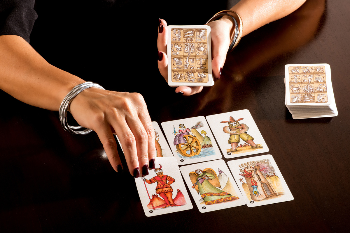 Mãos femininas organizando cartas de tarot em duas fileiras. 