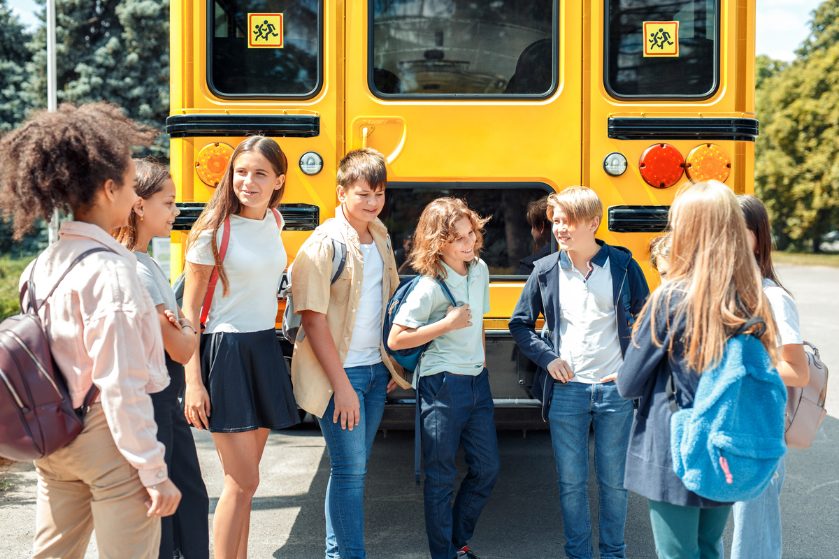 Crianças conversando com amigos em frente a ônibus de escola.