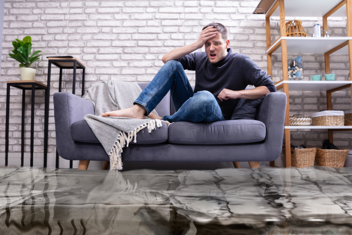 Homem no sofá assustado com sua casa inundada