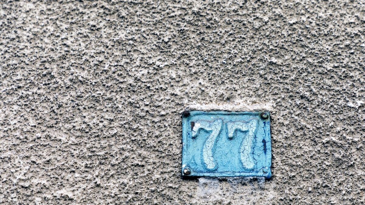 Número 77 em azul em parede cinza