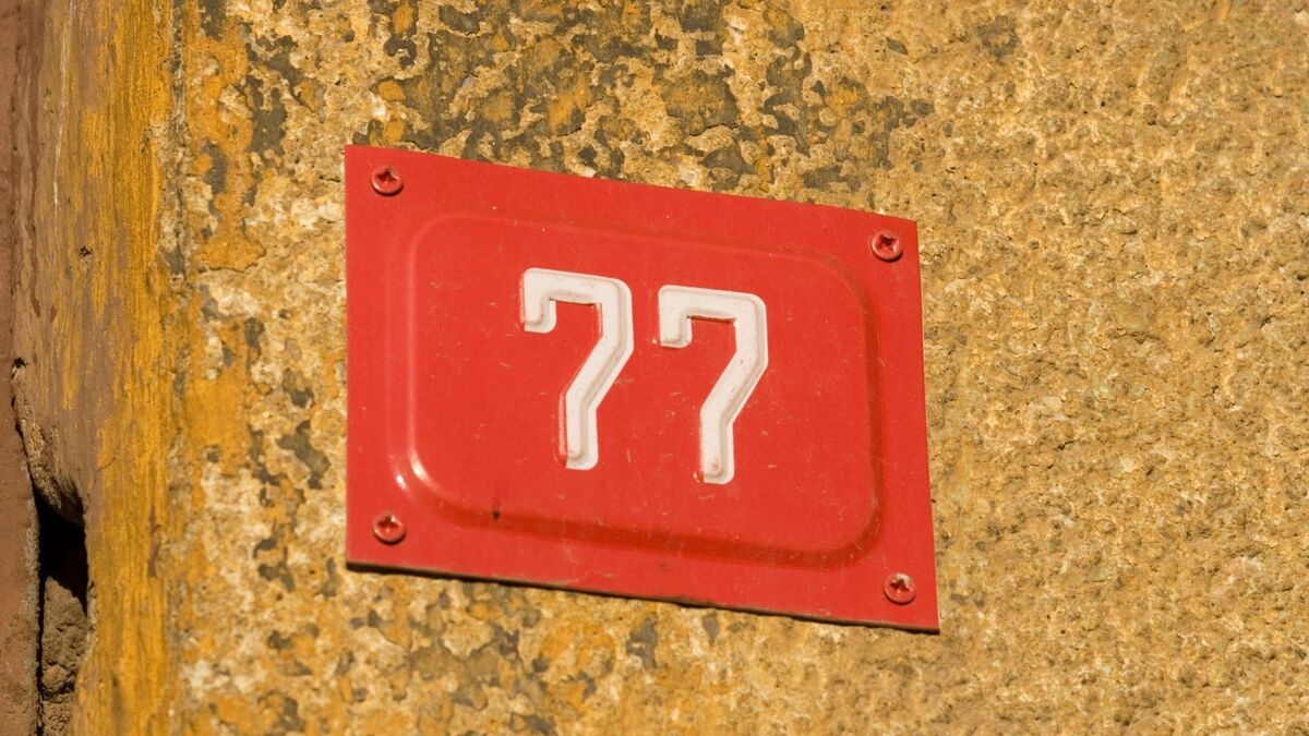 Número 77 em placa vermelha pregado em parede amarela