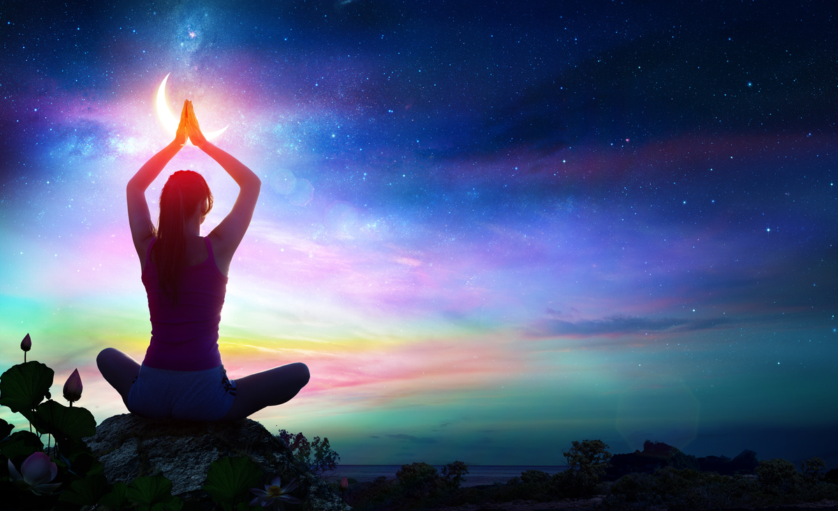 Pessoa meditando ao céu iluminado pelas cores dos 7 raios cósmicos.