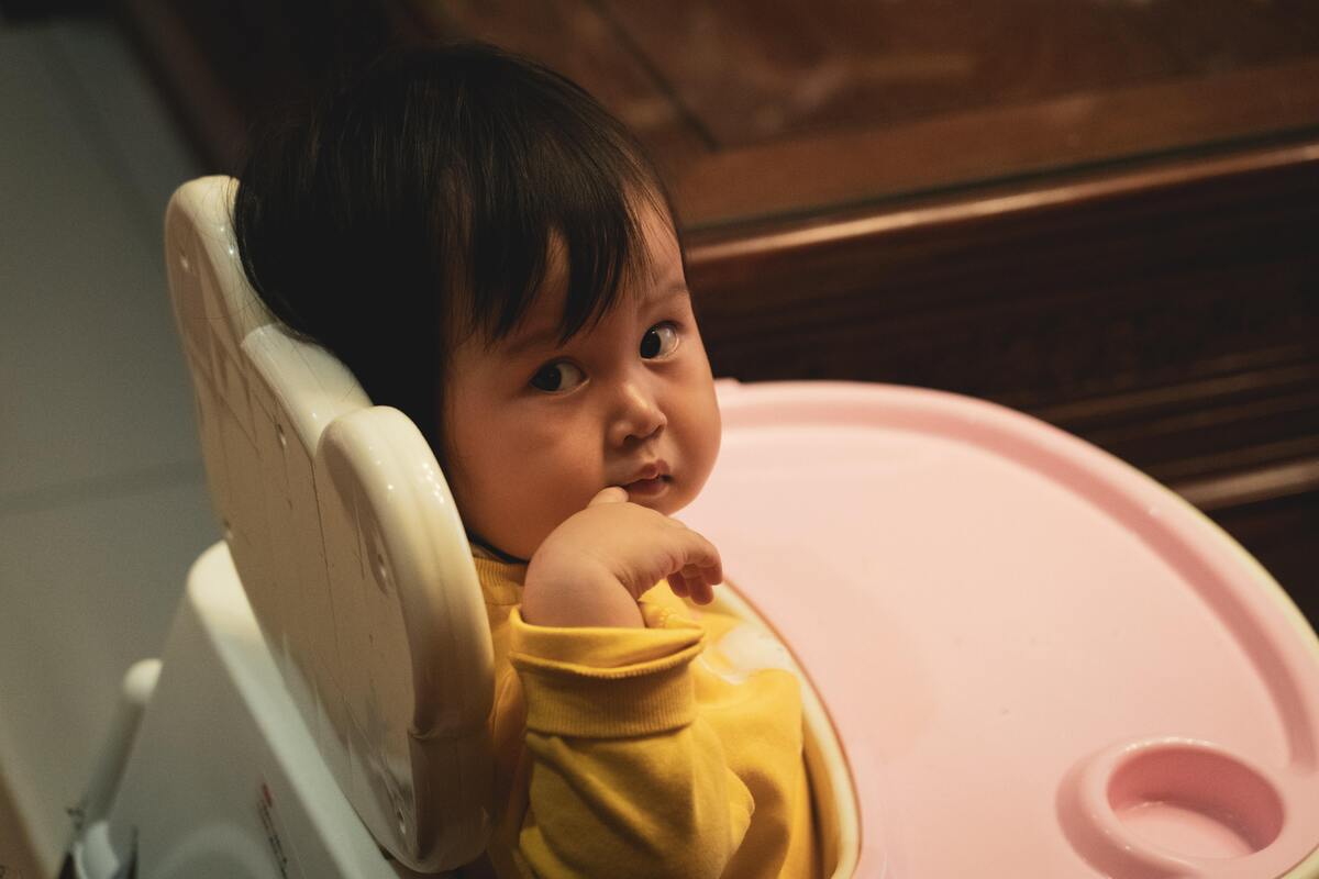 Criança sentada no alimentador com a mão na boca.