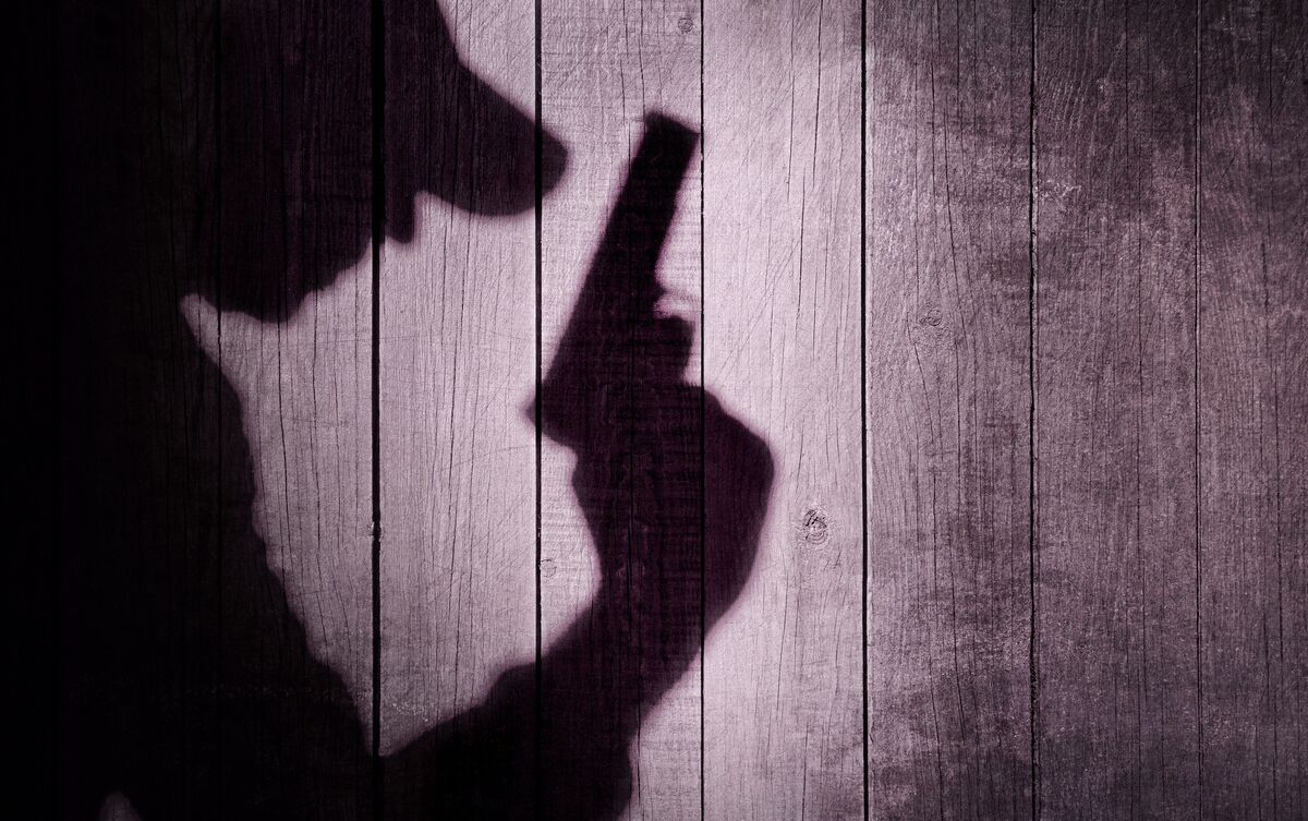 Sombra de assassino segurando arma de fogo na parede.