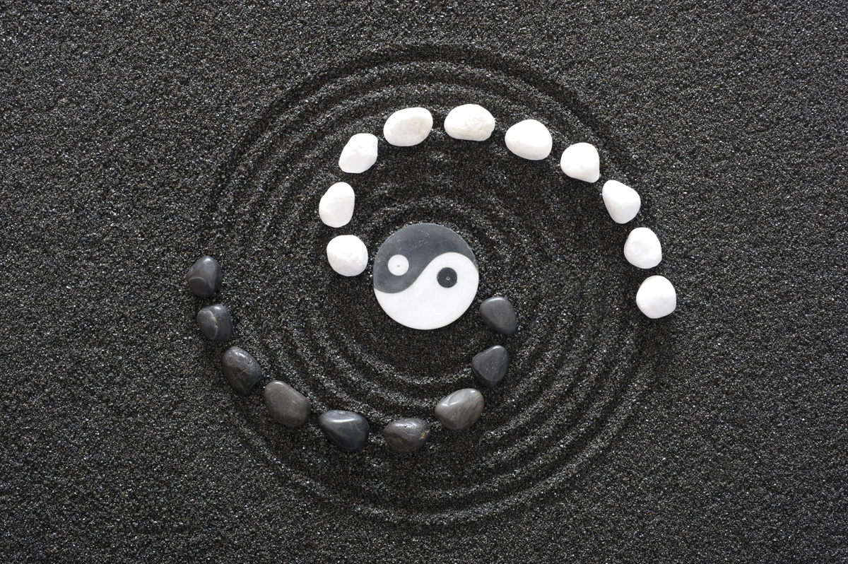 Símbolo do Yin Yang em areia com pedras em volta