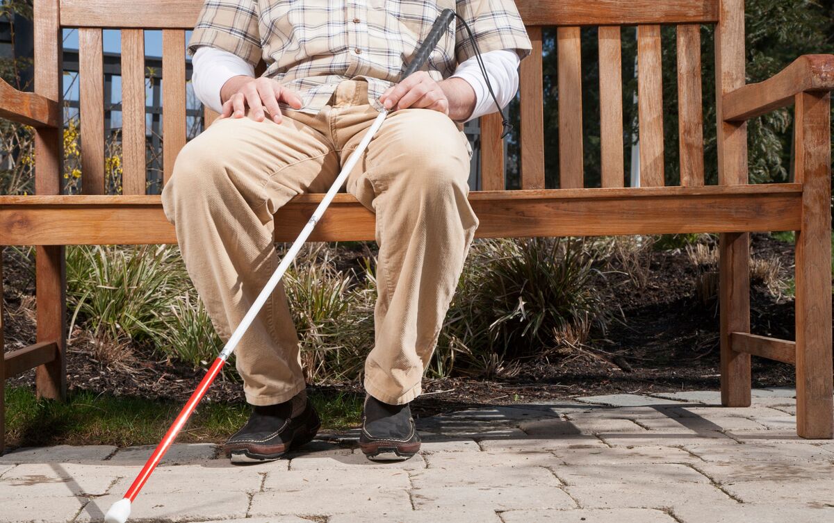 Homem cego sentado em banco de praça.