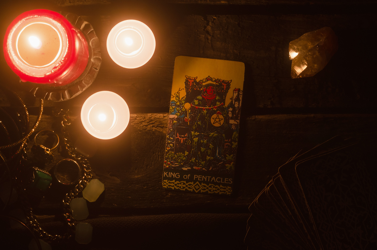 Carta Rei de Ouros do Tarot em altar com velas ao redor.
