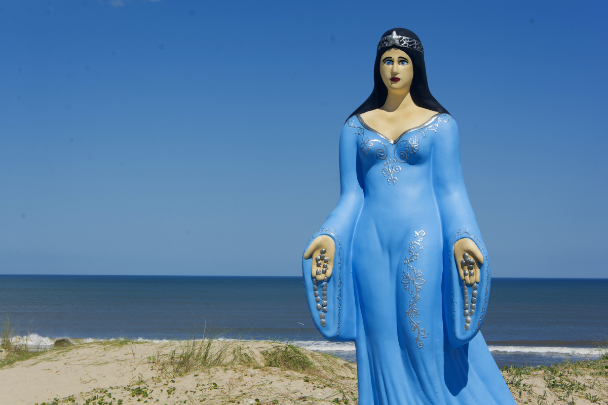 Estatua de Iemanjá com braços abertos na beira da praia. 
