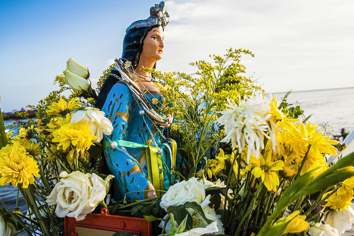 Estátua de Iemanjá rodeada de coroa de flores amarelas e brancas. 