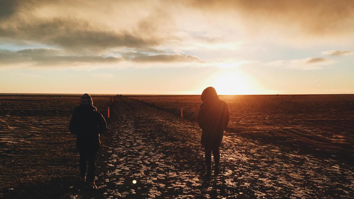 Duas mulheres andando em uma praia vazia no pôr do sol.