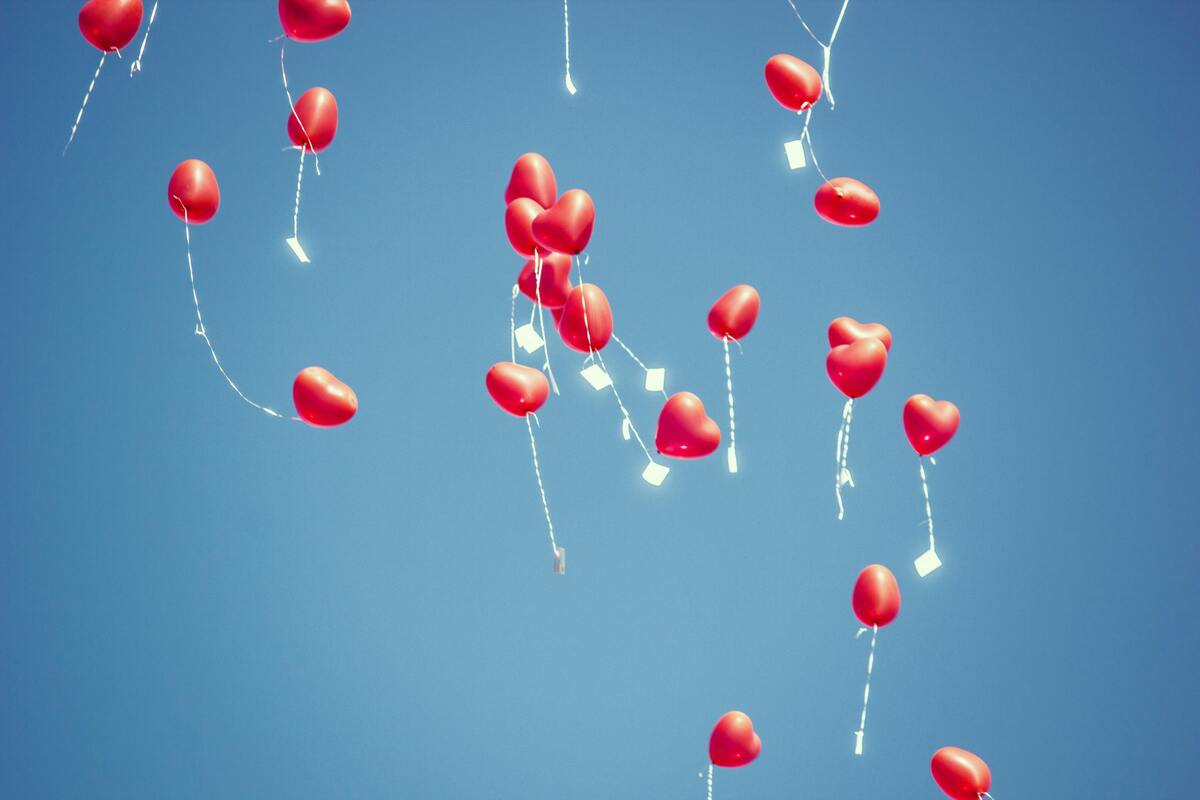 Balões em formato de coração no céu azul, carregando mensagens. 