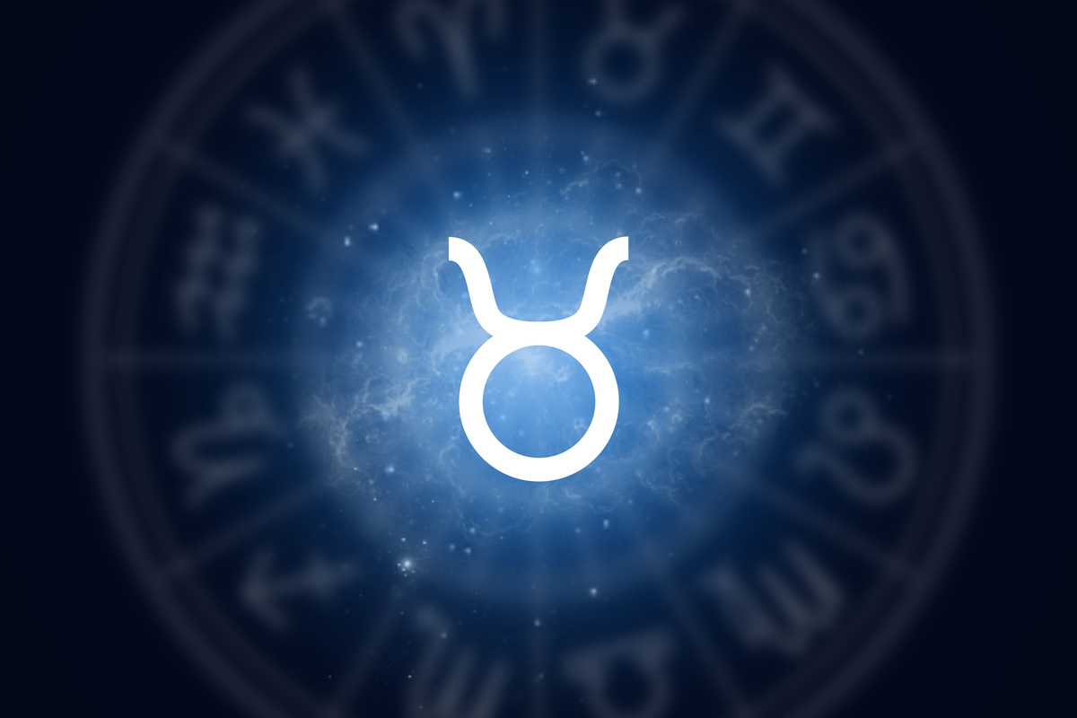 Símbolo do signo de Touro feito em traço azul-claro e iluminado, em fundo do céu azul-escuro e contornado por roda do mapa astral com pouca opacidade.