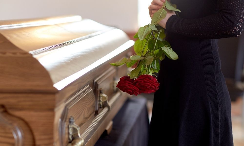 Mulher de luto ao lado de um caixão fechado com um morto dentro.