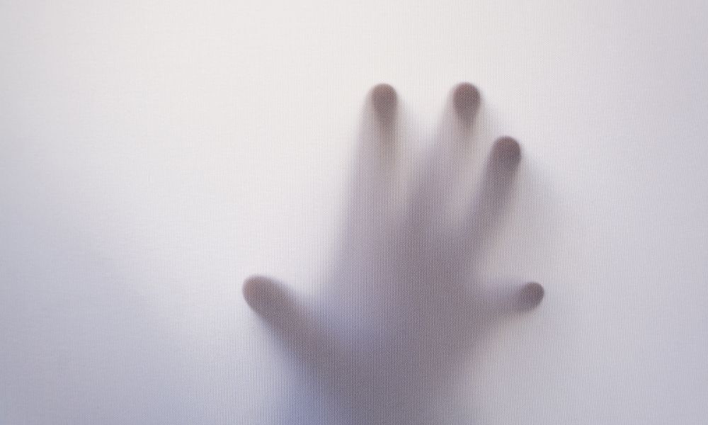 Mão atrás de um vidro desfocado branco. Uma mão espectral de um espírito de uma pessoa morta.