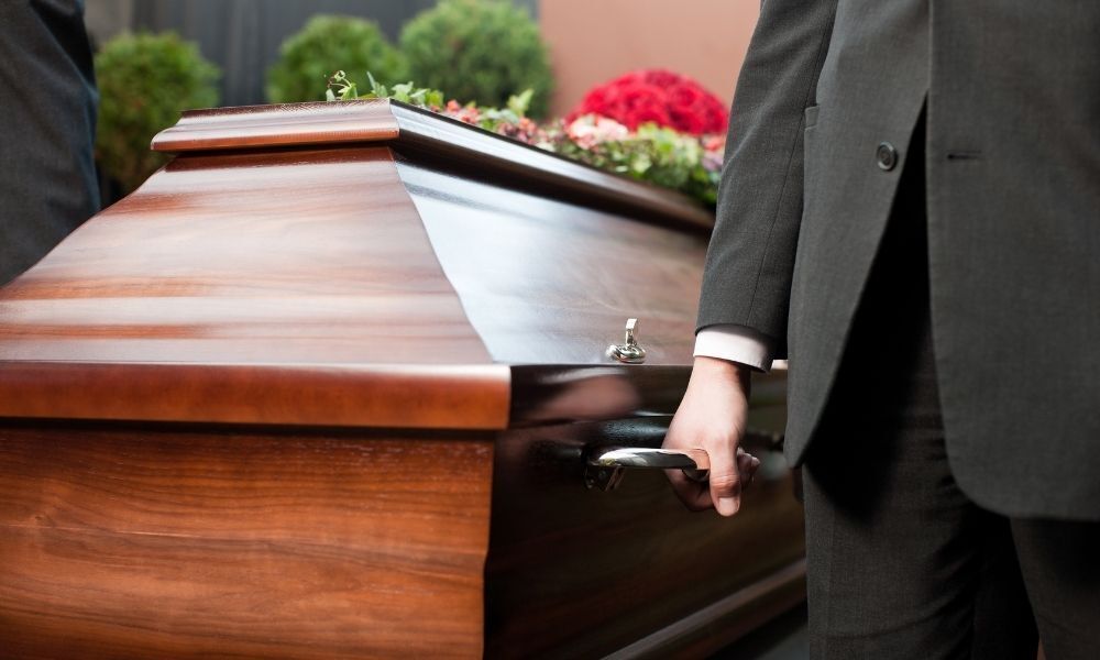Um homem carrega um caixão com alguém morto dentro.