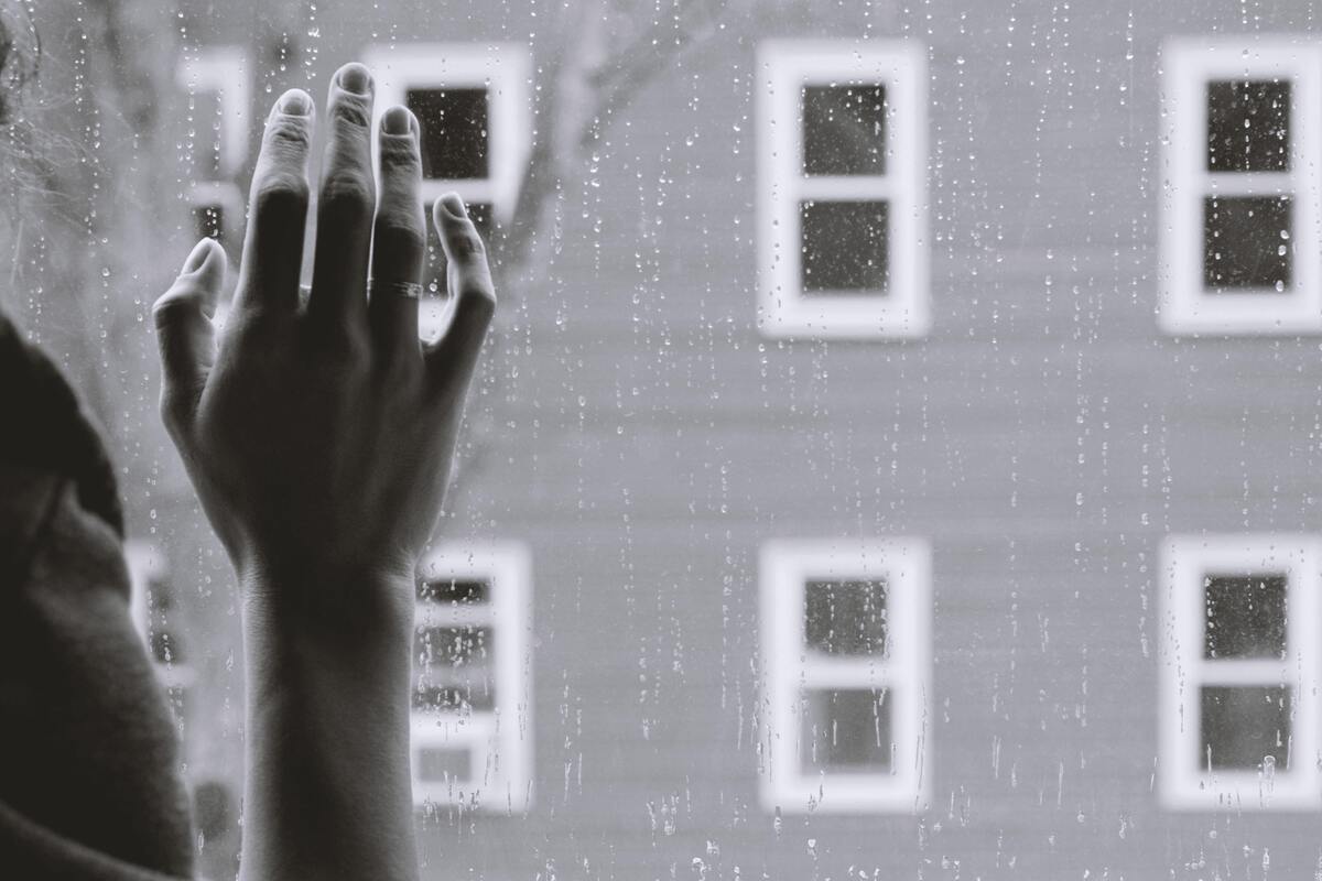 Mão feminina em uma janela tomada por pingos de chuva.