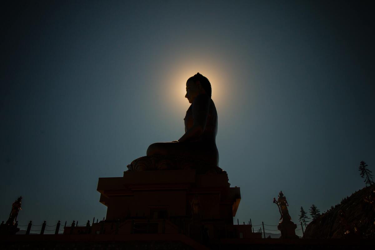 Silhueta de estátua meditando, sol ao fundo.