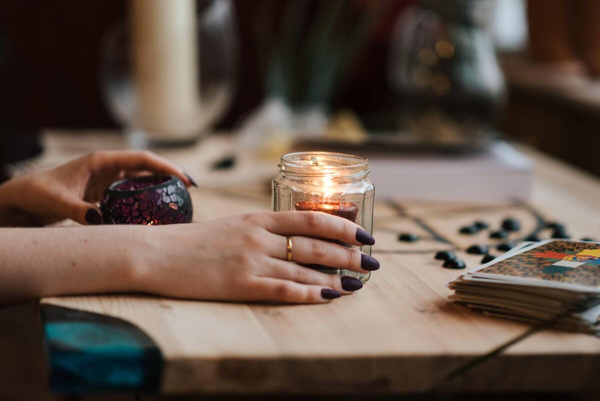 Mão segurando uma vela, ao lado de um baralho de tarot