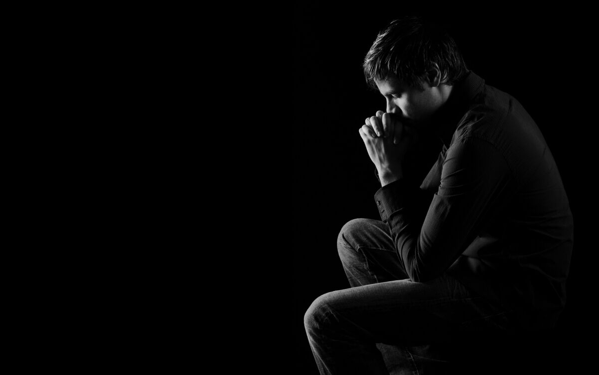 Homem sentado rezando no escuro.