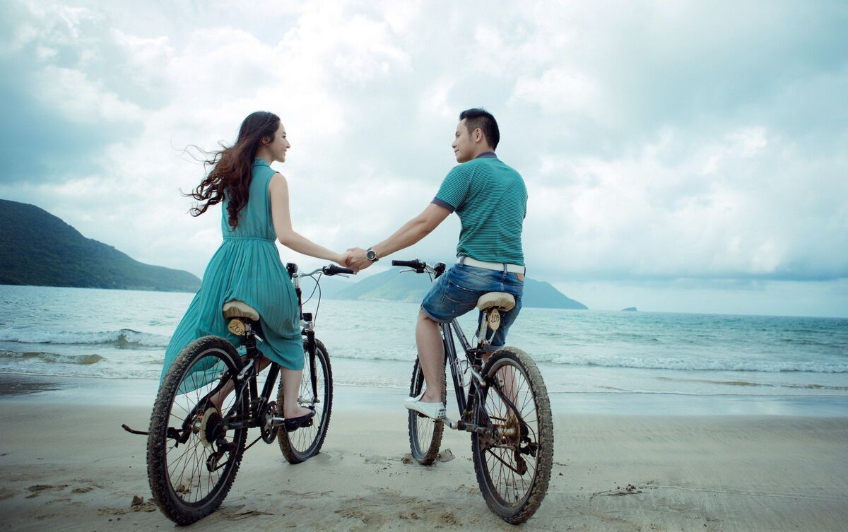 Casal de homem e mulher andando de bicicleta na praia.