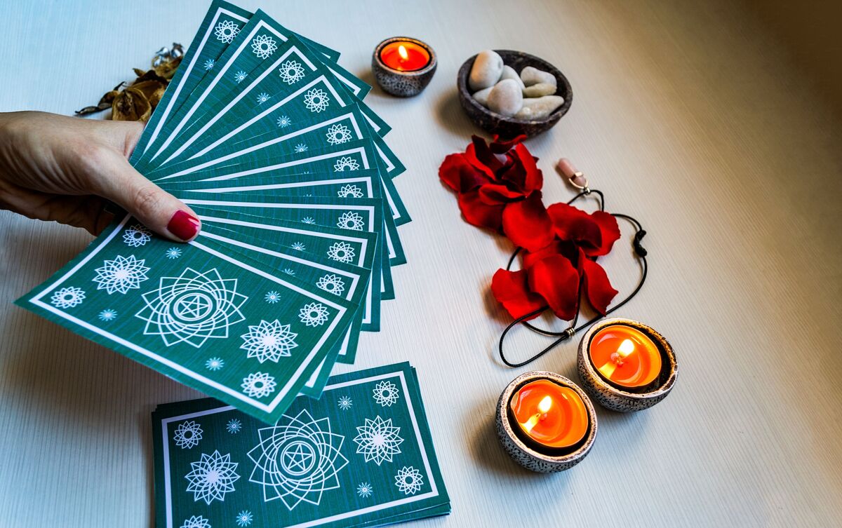 Mulher segurando deck de cartas de Tarot sobre mesa.