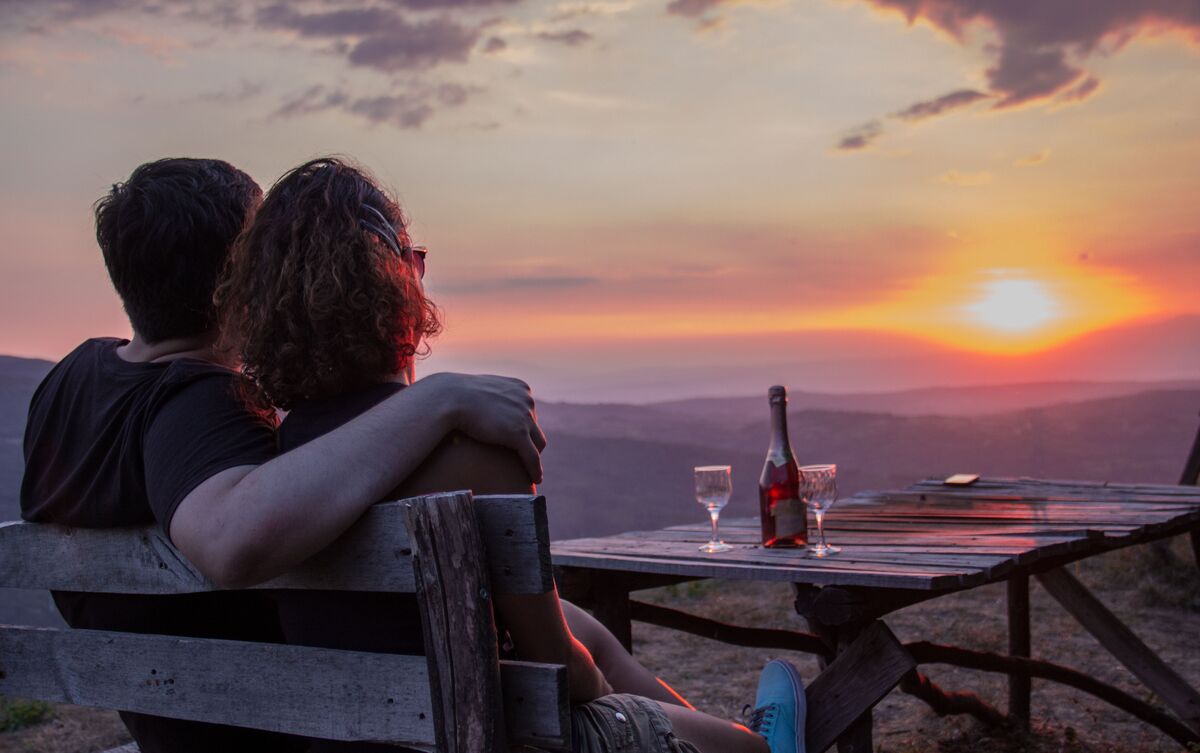 Casal de homem e mulher sentados em varanda observando o pôr do sol.