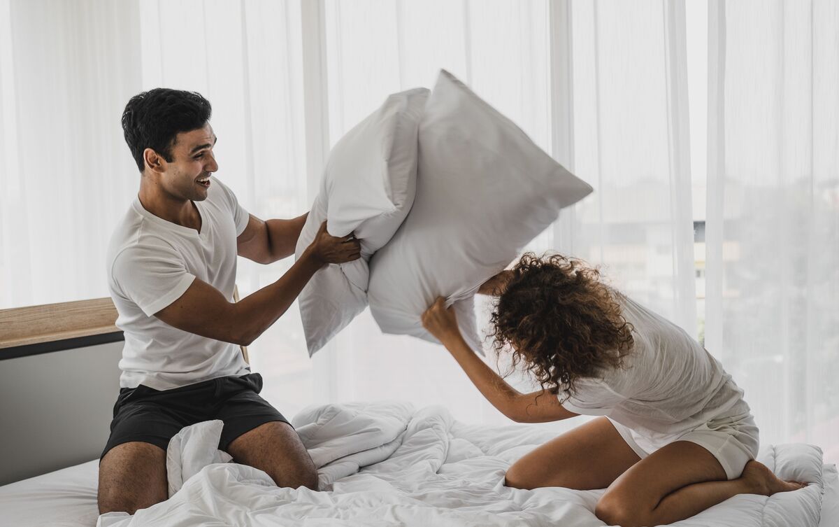 Homem e mulher brincando de guerra de travesseiros.