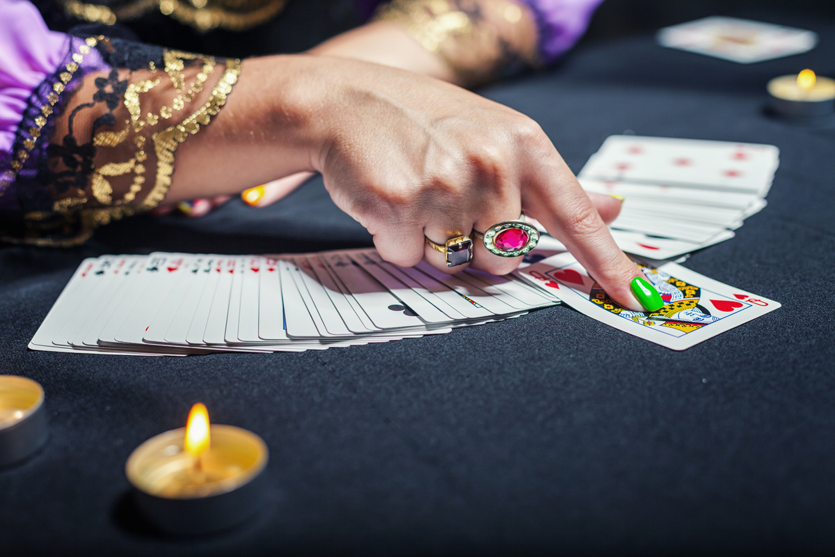 Mão com unhas pintadas apontando uma carta no baralho