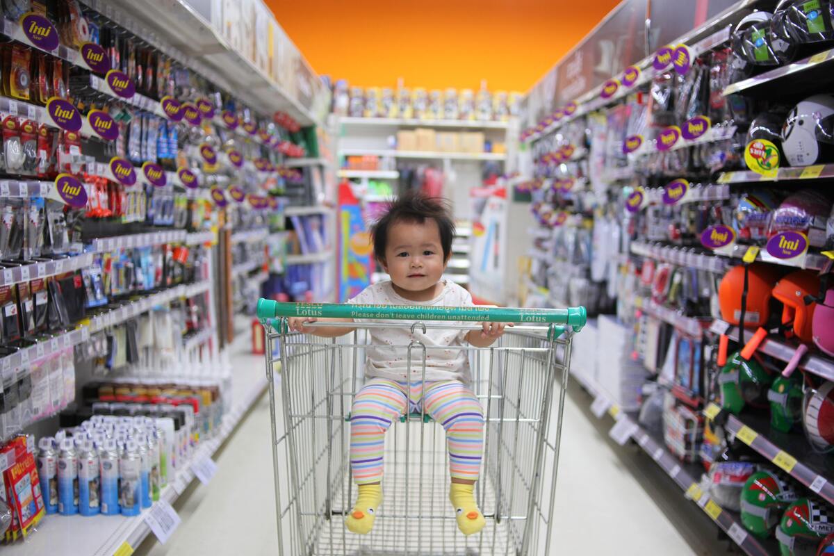 Uma criança dentro de um carrinho no corredor de um supermercado. 